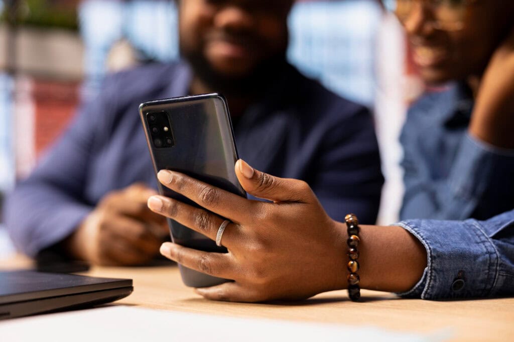 Two people looking at a phone being held in one's had with a ring on it.